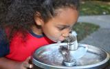 Niña bebiendo agua de una fuente pública