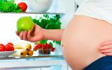 Mujer embarazada cogiendo una manzana del frigorífico