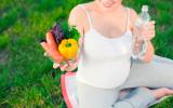 Una embarazada sostiene unas verduras y una botella de agua
