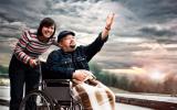 Una mujer sonriente empuja la silla de ruedas de un paciente con ELA