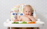 Un bebé en la trona come trozos de verduras cocidas que tiene delante