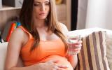 Mujer embarazada sostiene un vaso de agua con gesto preocupado