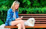 Una joven consulta en su móvil dónde puede ir con su perrito, tumbado junto a ella