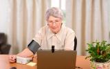 Una anciana se toma la tensión en casa frente a la pantalla de un ordenador