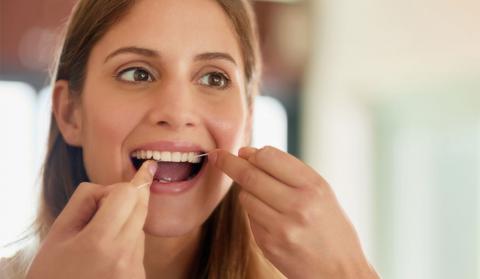 Una mujer usando hilo dental para limpiarse la dentadura