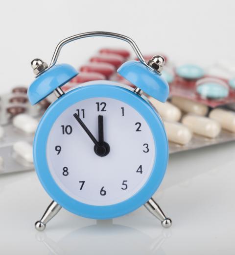 Reloj azul marca casi las 12 y detrás varios blíster de medicamentos