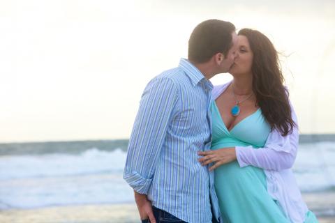Una mujer embarazada besa a su pareja en una playa