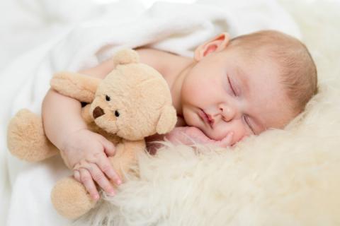 Bebé durmiendo con la mejilla apoyada en la mano y abrazando a su osito de peluche