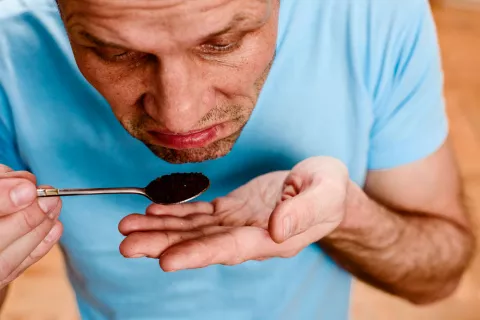 A man trying to smell a spoonful of coffee