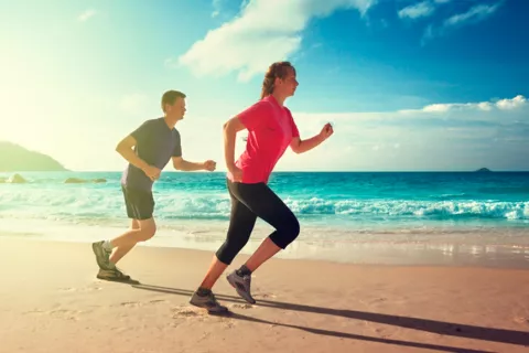 Pareja corriendo bajo el sol por la playa