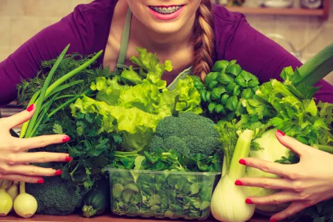 Fibermaxxing: pros y contras de maximizar tu ingesta de fibra Mujer joven sosteniendo entre sus brazos un monto de vegetales distintos
