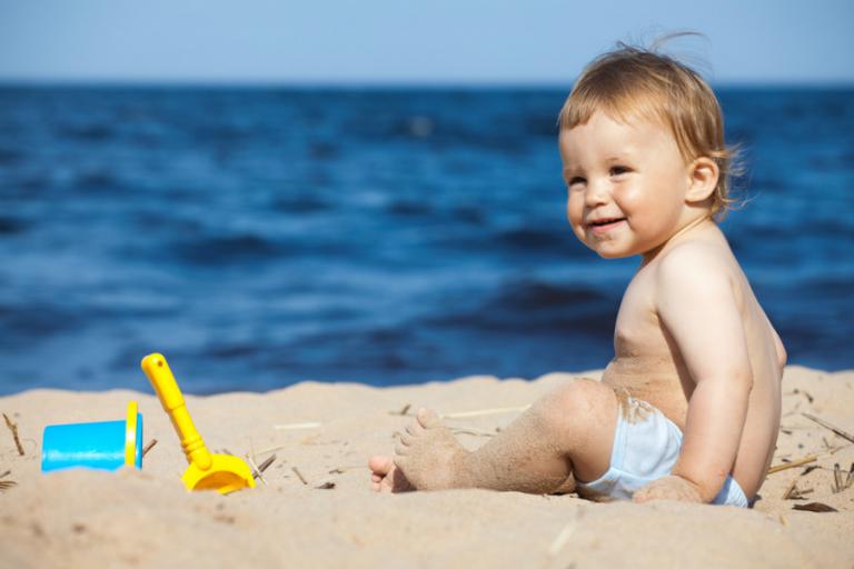Bebé sentado en la arena junto al mar