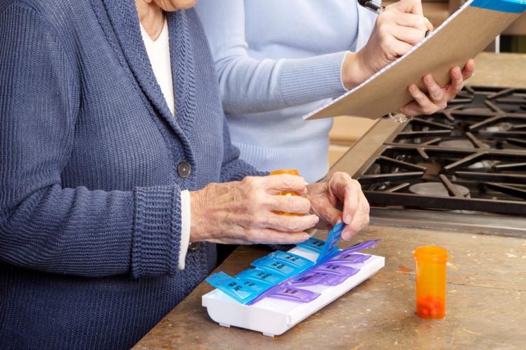 Una cuidadora ayuda a una anciana a organizar su pastillero