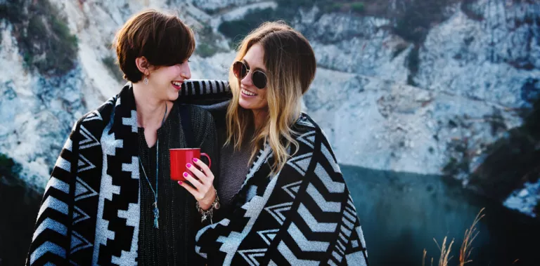 Dos mujeres debajo de una manta tomando una taza de café caliente