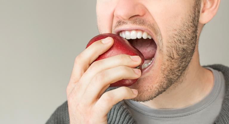 Hombre mordiendo una manzana para prevenir el sarro dental
