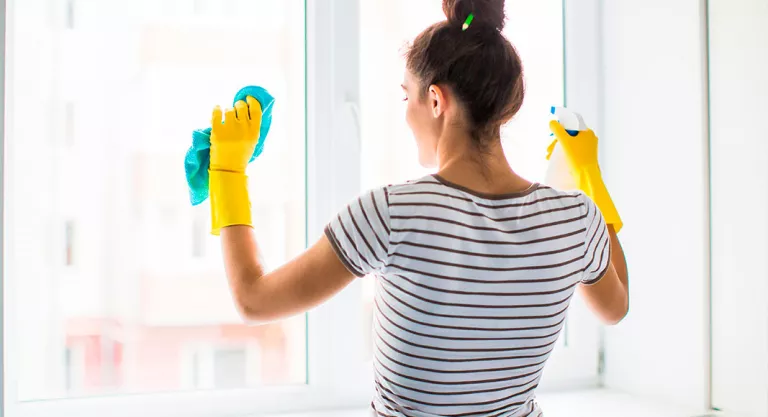 Chica limpiando los cristales de su casa