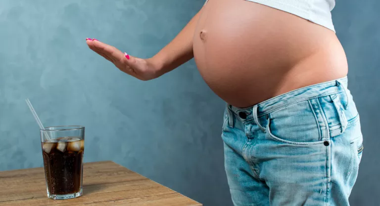 Embarazada rechazando un vaso de cola por tener cafeína