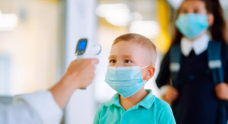 Midiendo la temperatura corporal de un niño con mascarilla