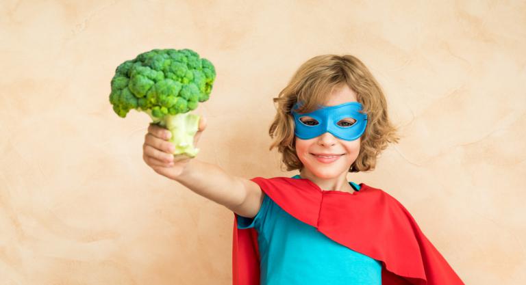 Niño vestido de super heroe con un brócoli en la mano