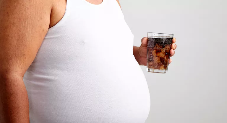 Hombre con obesidad sosteniendo un vaso de Coca-Cola