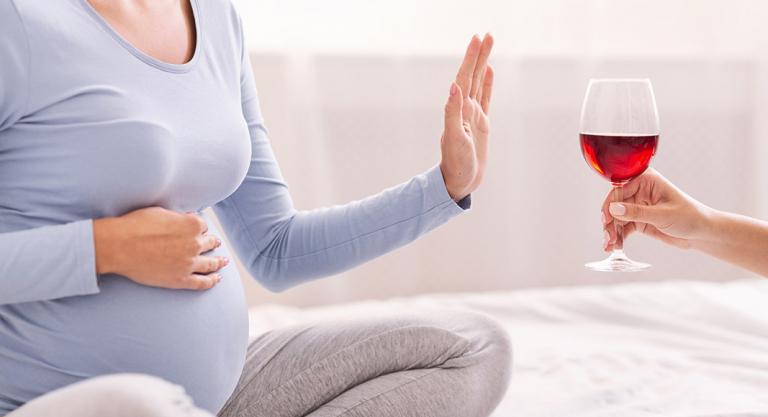 Embarazada rechazando una copa de alcohol y así evitar la migraña 