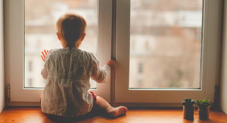 Niño mirando la calle desde la ventana de su habitación