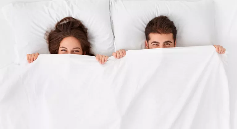 Pareja sonriendo bajo las sábanas en la cama