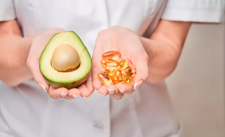 Mujer sosteniendo un aguacate y cápsulas de omega 3