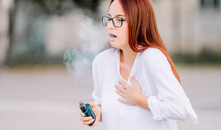 Una mujer tosiendo con un vapeador en la mano