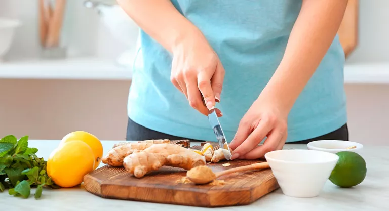 Mujer cortando una raíz de jengibre para preparar un plato de comida