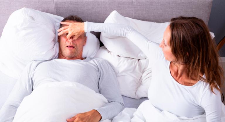 Mujer tapando la nariz a su marido para evitar que ronque en la cama