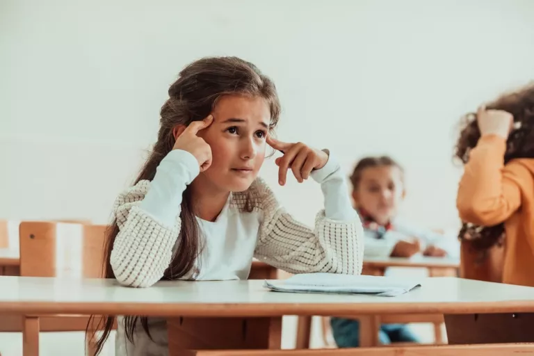 Niña sentada en el pupitre del colegio con cara de frustración