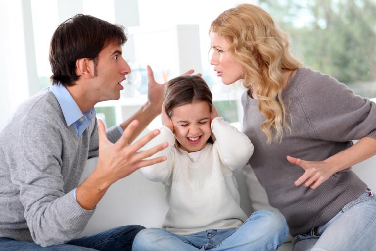 Dos padres discutiendo en el sofá con su hija en medio de ellos