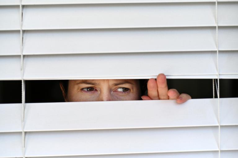 Persona escondida mirando por un hueco entre las cortinas