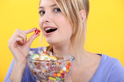 Una mujer sostiene un bol lleno de caramelos, a punto de comerse uno
