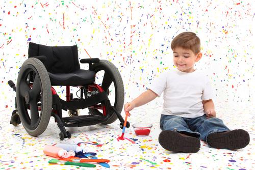 Niño pequeño pintando en el suelo junto a su silla de ruedas