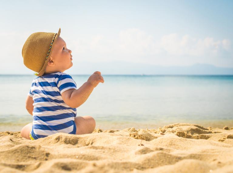 Bebé en la playa protegido del sol con un sombrero