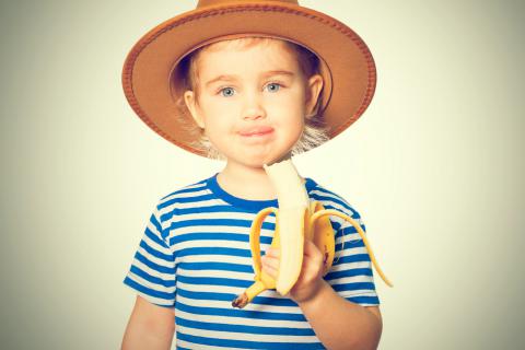 Una niña sostiene un plátano que se está comiendo
