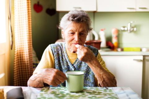 Una mujer mayor se toma un suplemento nutricional en la cocina de su casa