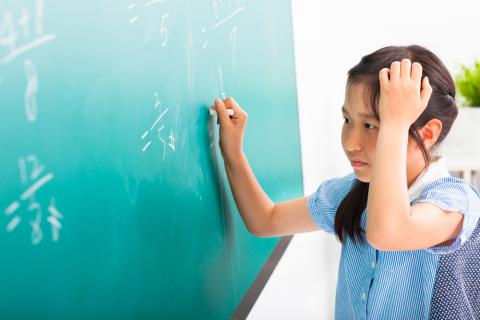 Una niña intenta resolver un problema matemático en la pizarra