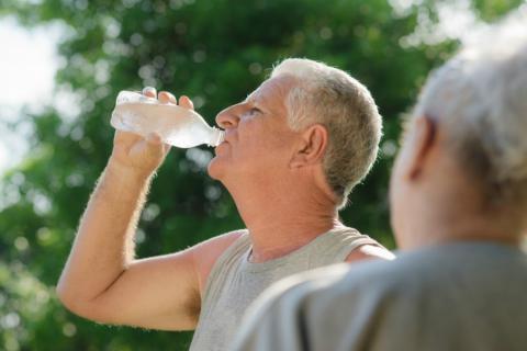 Un adulto mayor bebe agua tras una sesión de ejercicio al aire libre