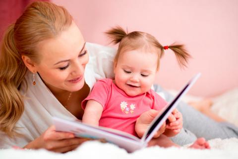 Una niña pequeña manipula un libro infantil junto a su madre