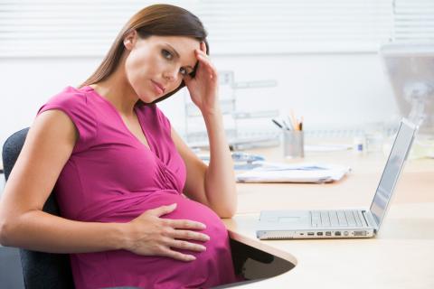 Mujer embarazada sentada frente al ordenador en su puesto de trabajo