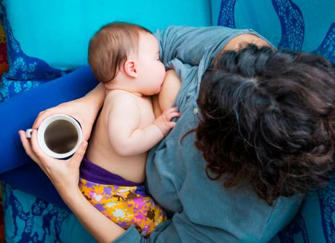 Mujer tomando café y dando el pecho a su bebé