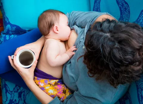 Mujer tomando café y dando el pecho a su bebé