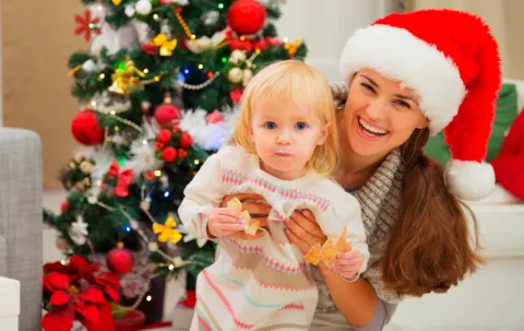 Madre sosteniendo a su bebe comiendo junto al árbol de navidad