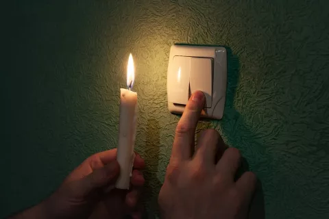 Concepto de apagón eléctrico masivo Un hombre intenta encender un interruptor con una vela en la otra mano