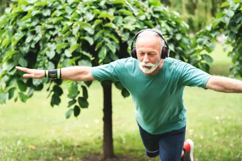 Prueba de equilibrio a una prueba para comprobar cómo envejeces Hombre de edad avanza hace equilibrio sobre una sola pierna en un jardín escuchando música