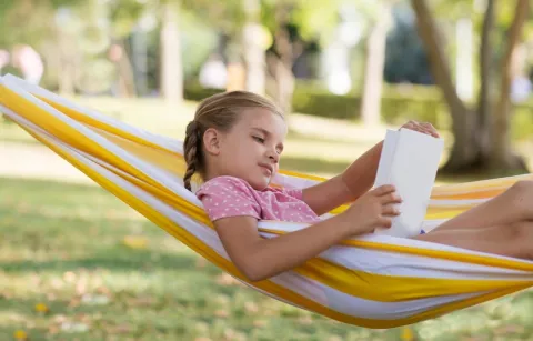 Aprender durante las vacaciones sin ir a la escuela Nia rubia tumbada en verano en una hamaca leyendo un libro