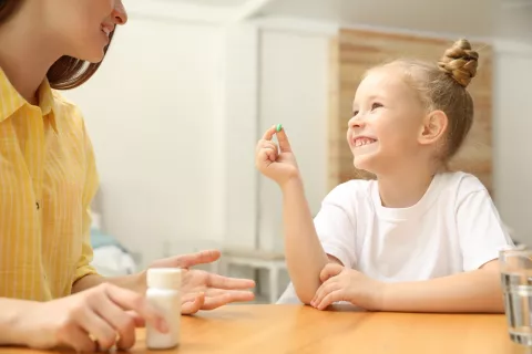 Suplementos vitamínicos en los niños Madre le da una vitamina a su hija pequeña que la coge sonriendo
